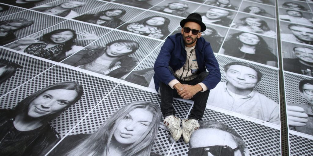 Lo street artist francese JR seduto su una delle sue opere site specific